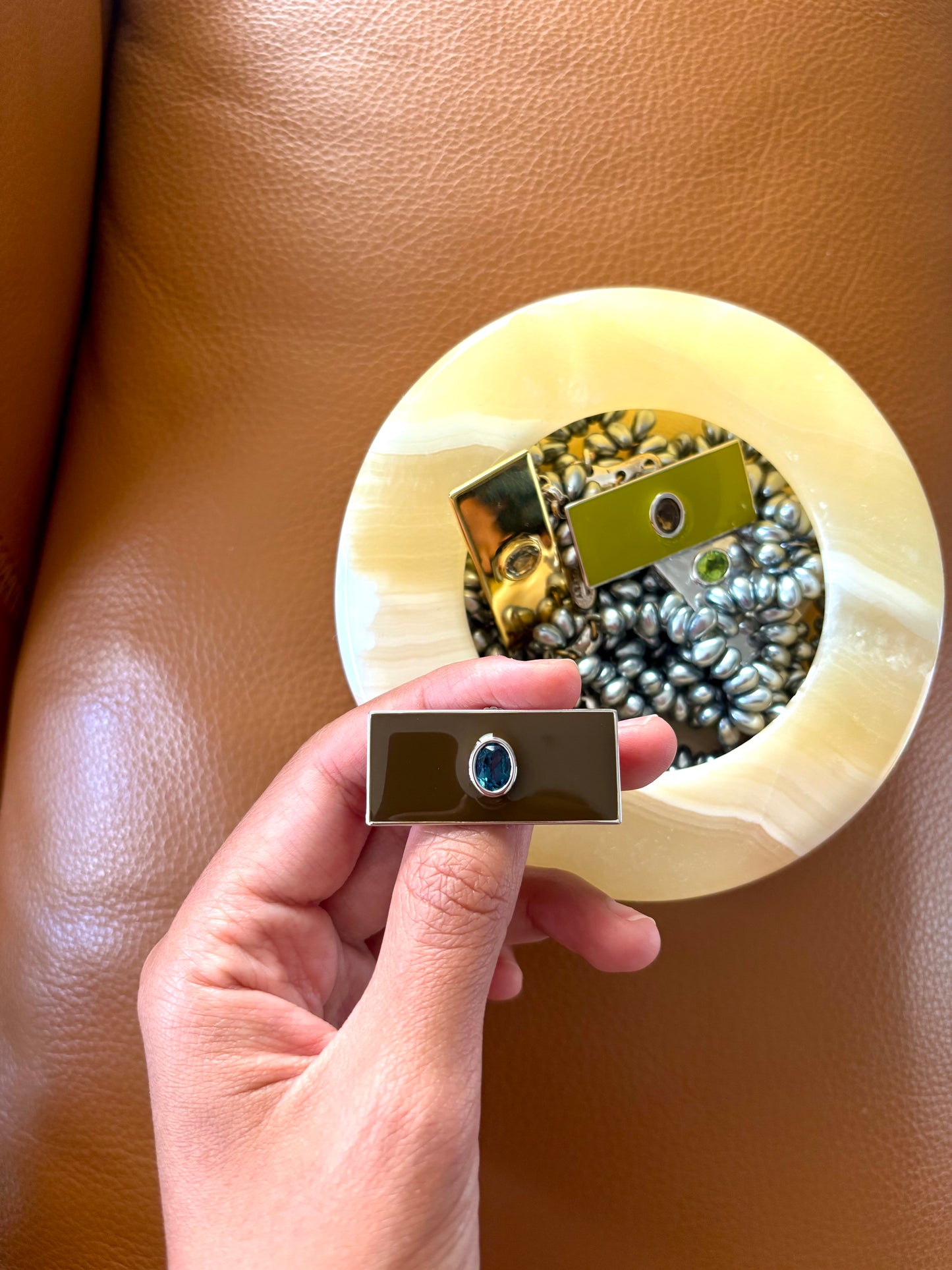 Hand holding a small rectangular earring with an oval gem on a beige background